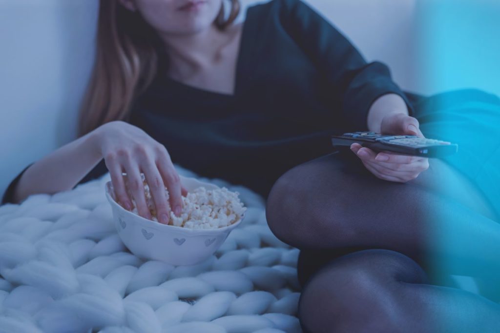 woman eating popcorn while holding tv remote control