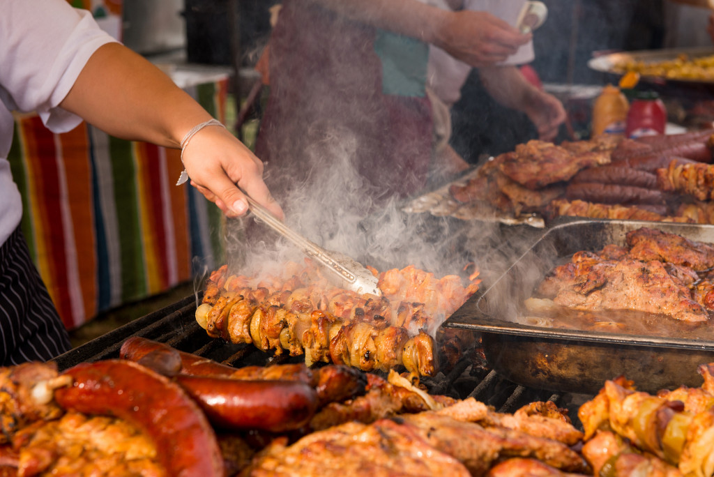 People cooking various meats on a barbecue grill